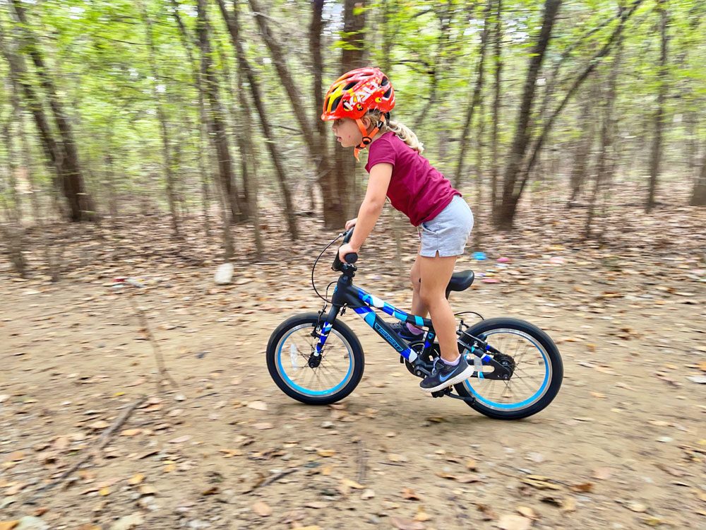 Child riding down dirt path on Guardian 16 inch bike, standing up on pedals