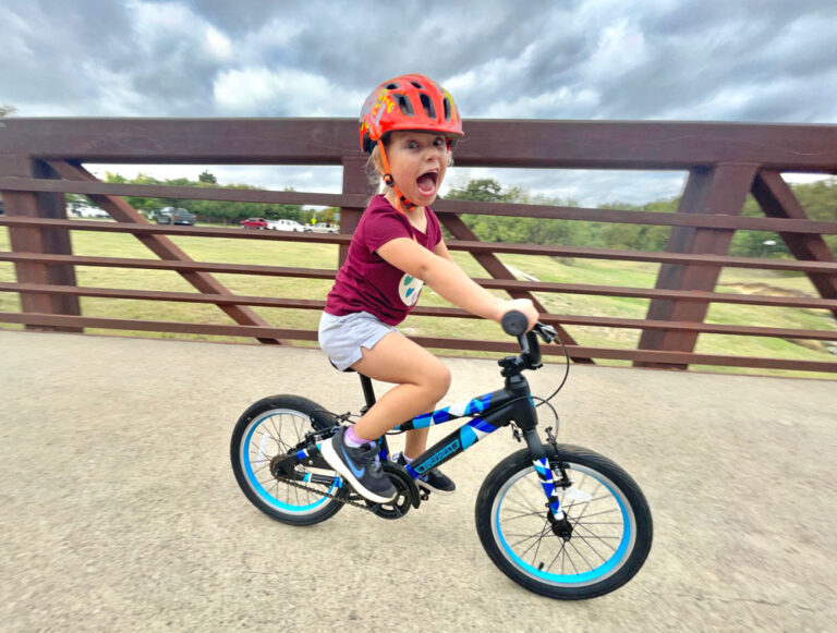 Child riding Guardian 16 inch bike across a bridge and making a funny face