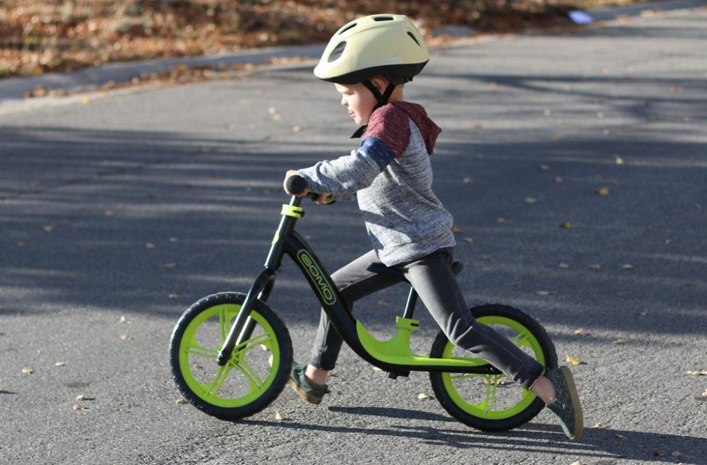 boy riding a green and black gomo balance bike