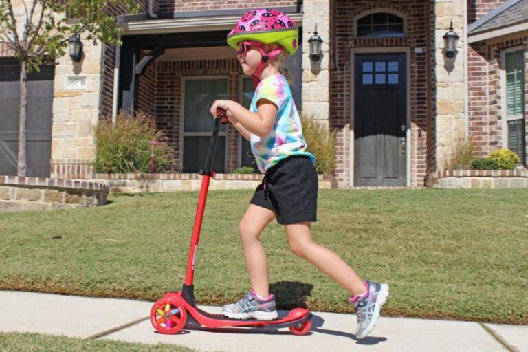 a young girl riding a red 3 wheeled scooter