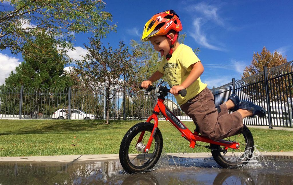 boy riding a red balance bike through a puddle