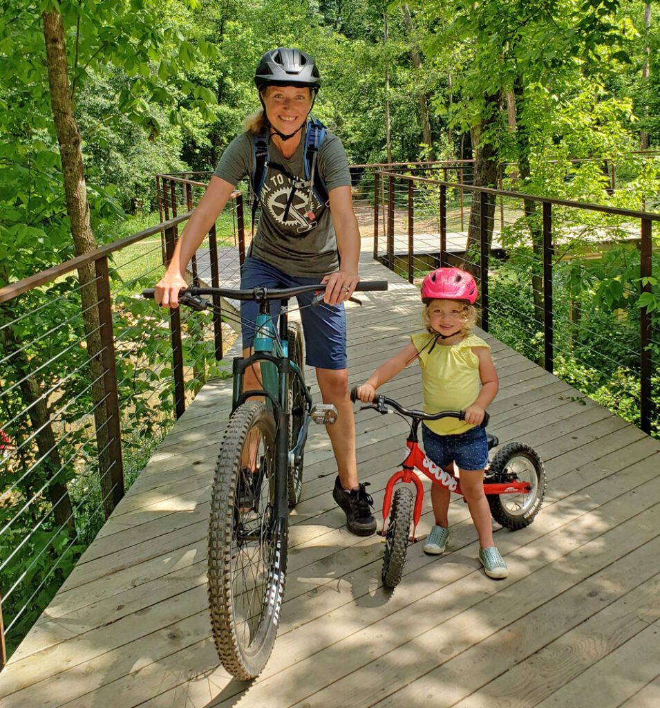 Mom on mountain bike with 2 year old toddler on balance bike next to her