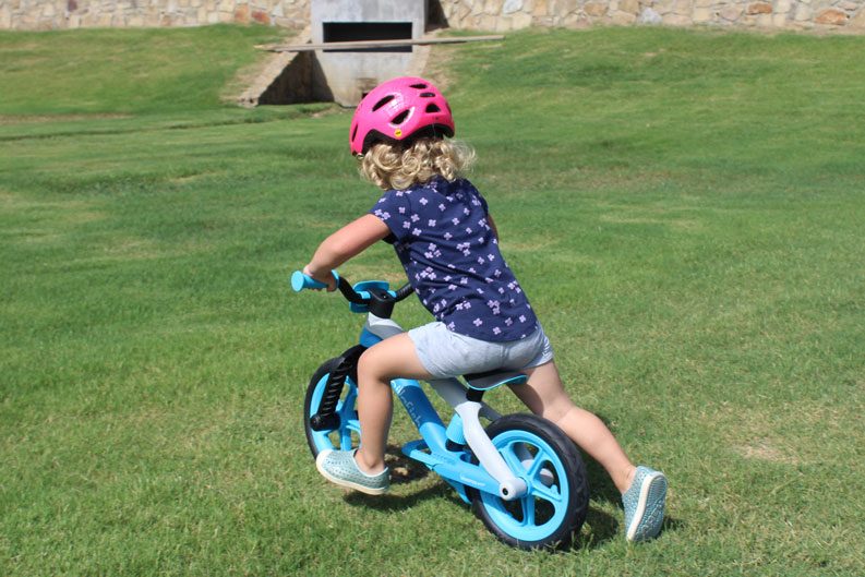Toddler riding Chillafish BMXie2 balance bike, running at full speed across the grass
