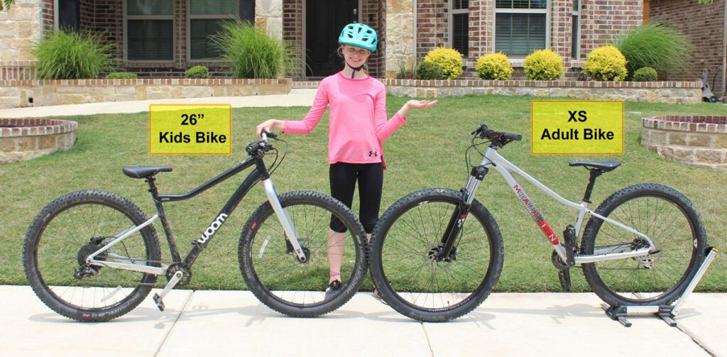 11 year old girl standing between a 26 inch bike for kids and an XS adult bike