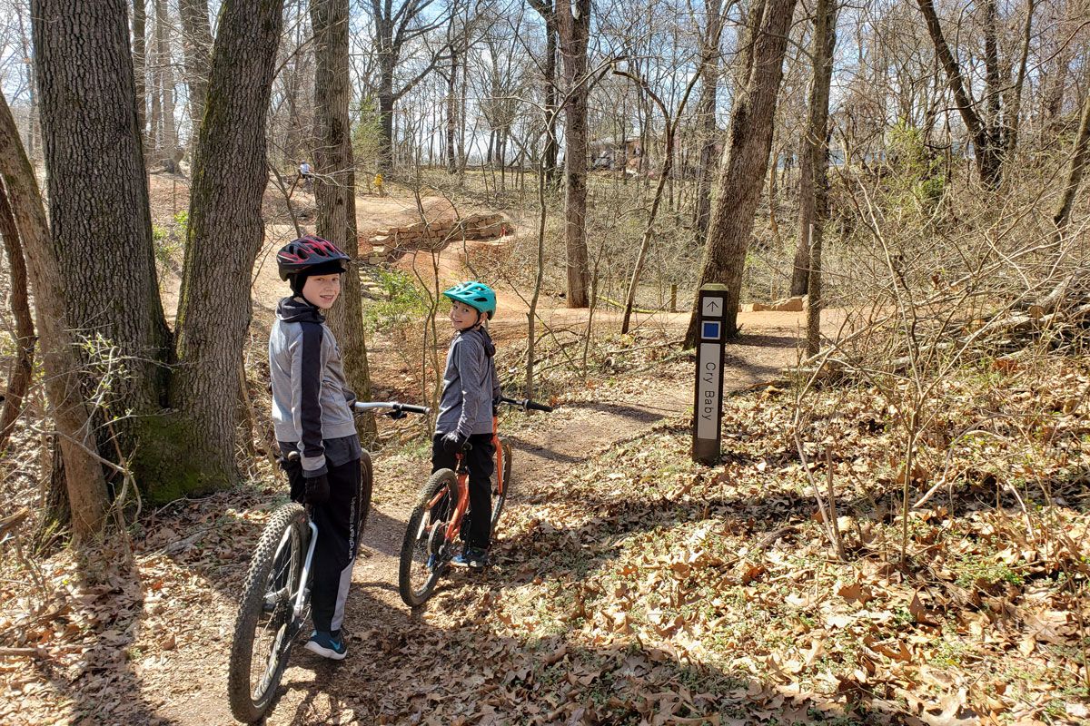 Two boys riding mountain bikes at trail head of Cry Baby at Slaughter Pen in Bentonville Arkansas