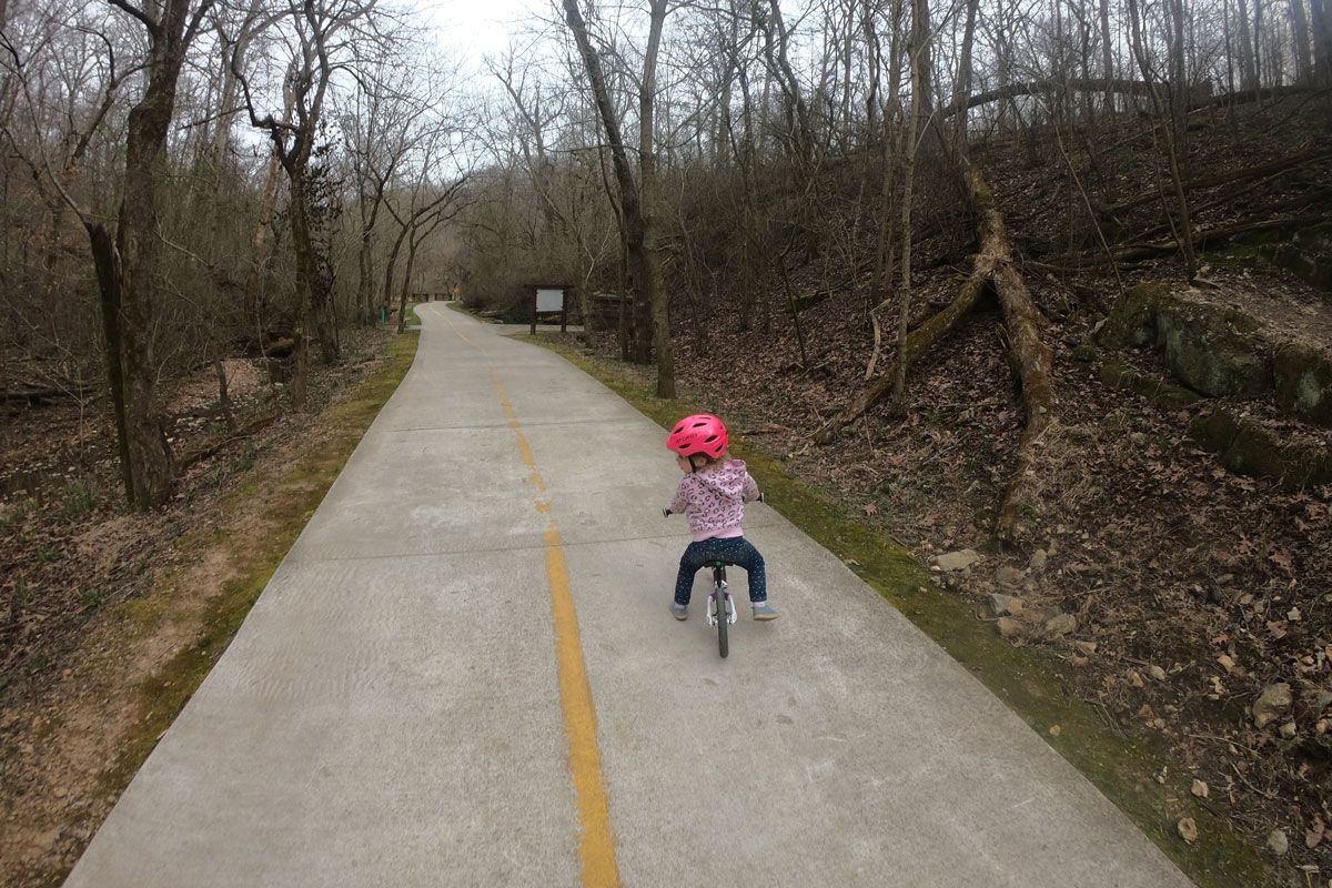 Toddler riding balance bike on paved trail to Lake Atalanta in Arkansas.