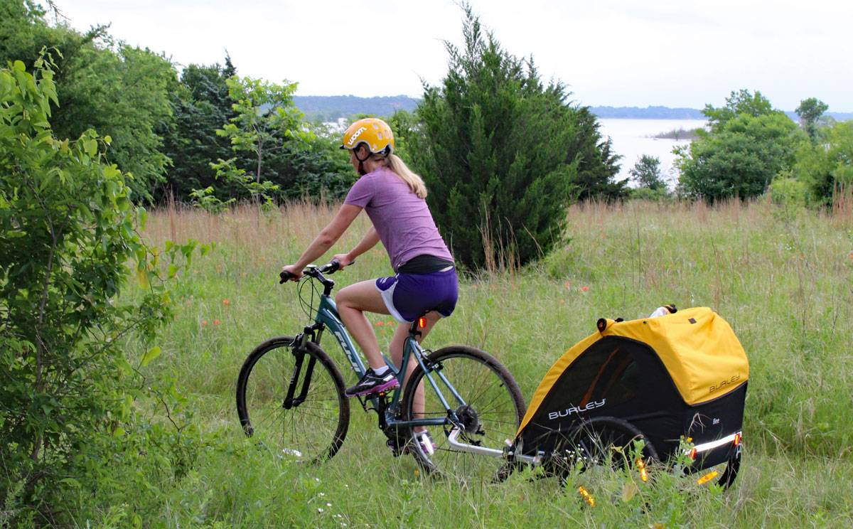 Mom pulling toddler in Burley Bee bike trailer. Through grassy trail.