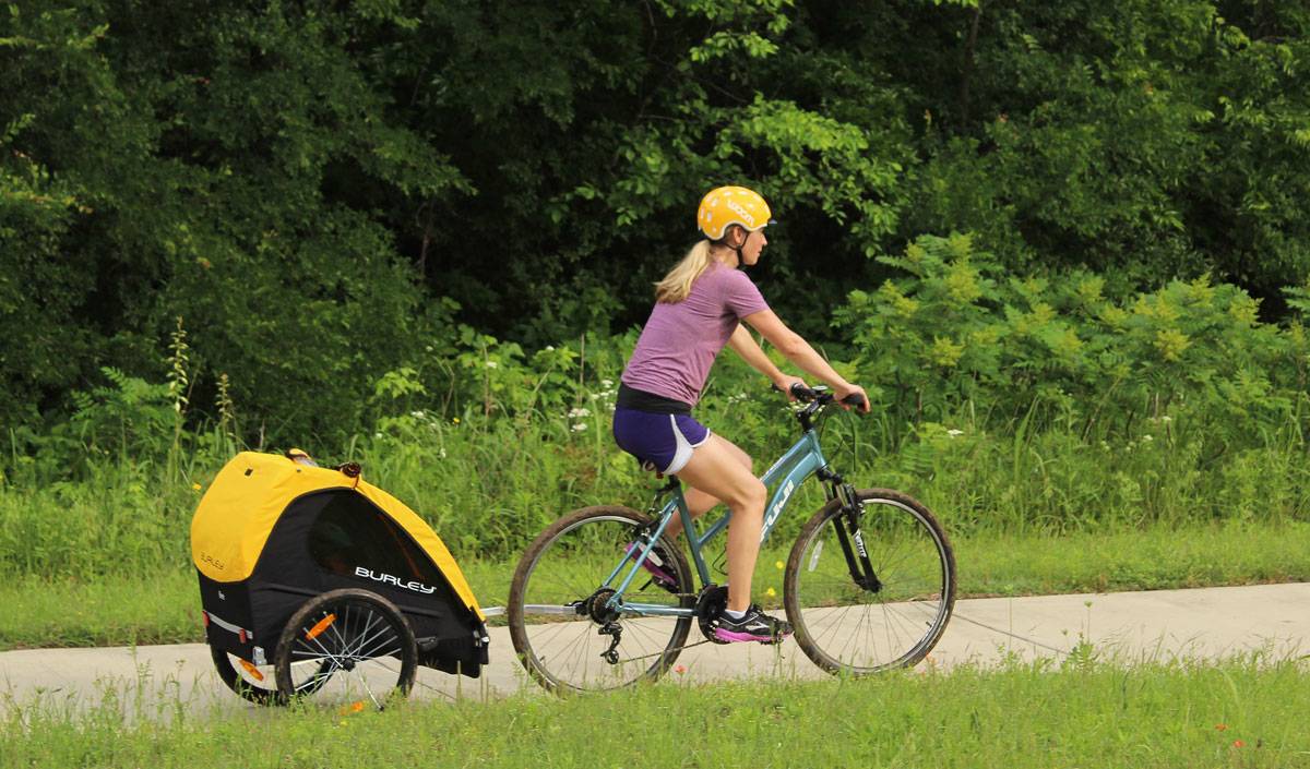 Mom pulling toddler in Burley Bee bike trailer. Paved trail.