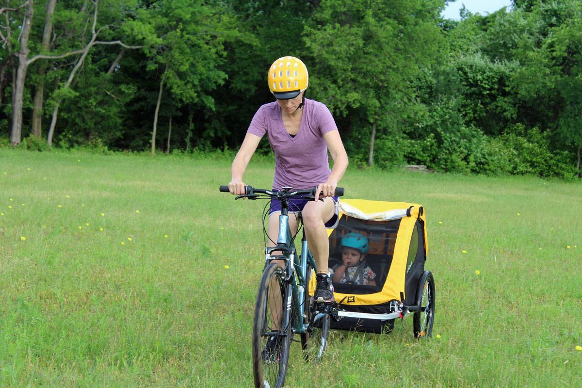 Mom pulling toddler in Burley Bee bike trailer. Through meadow