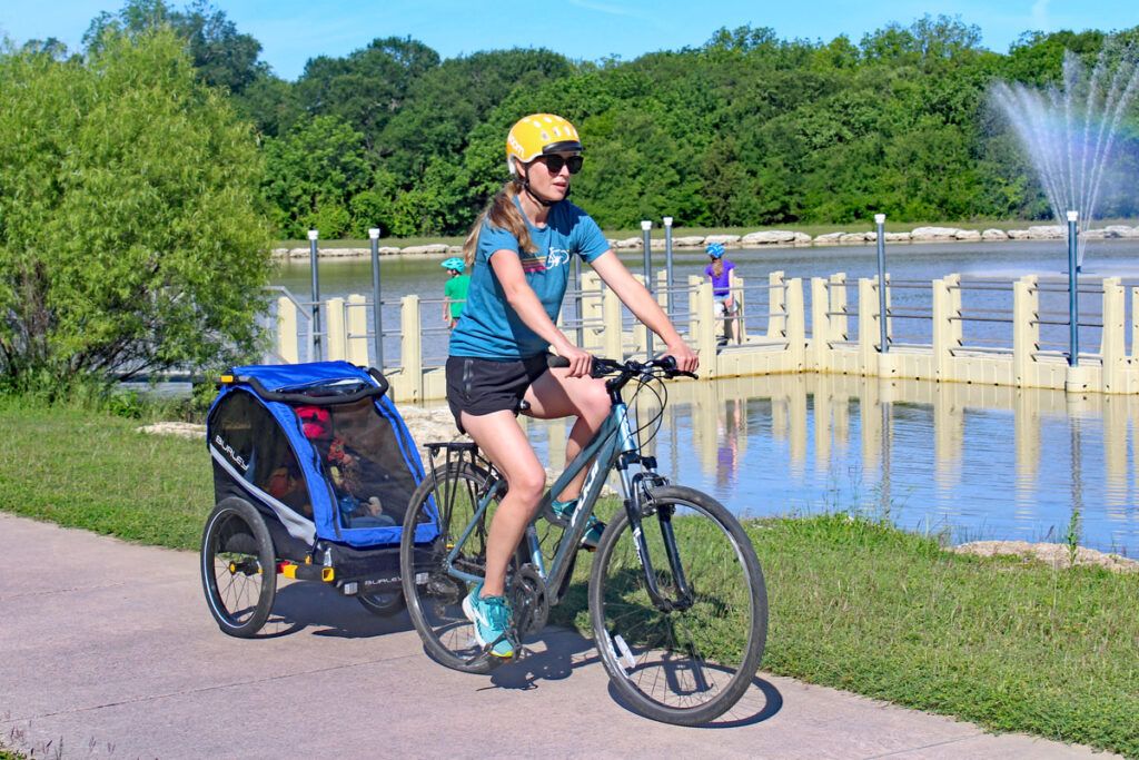 mom pulling the burley dlite kids bike trailer behind her bike