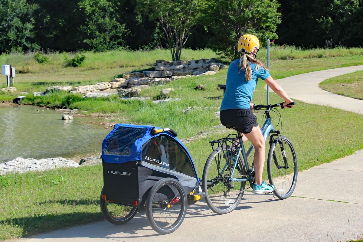 Mom riding down paved path pulling Burley D'Lite bike trailer