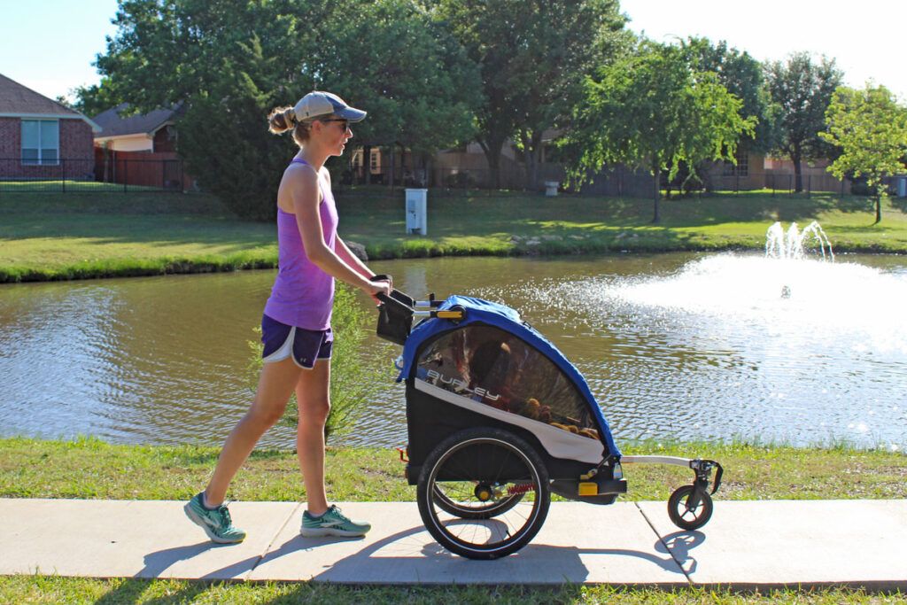 Mom pushing Burley DLite Single trailer stroller by a lake