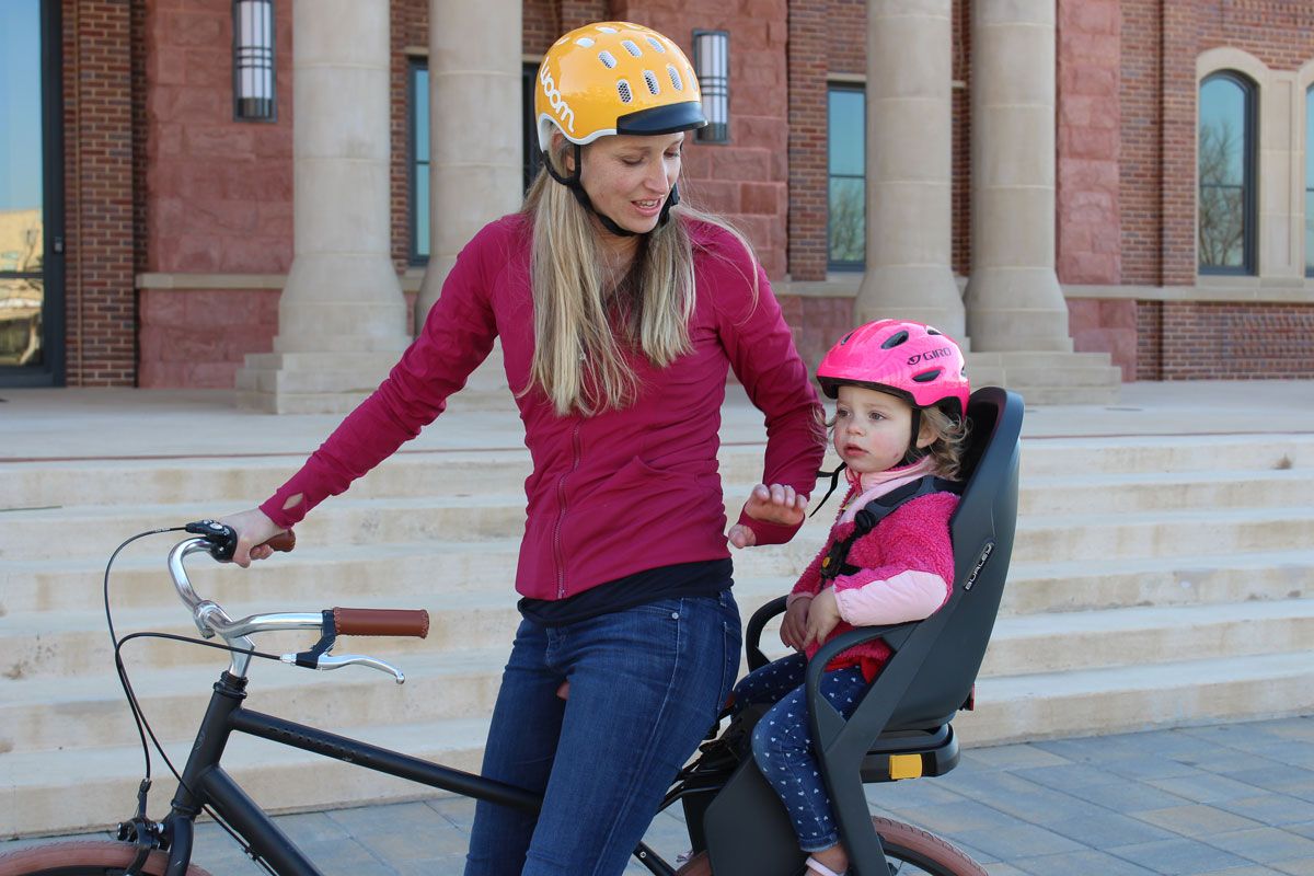 Mom smiling on bike with 2 year old toddler sitting in the Burley Dash child bike seat.
