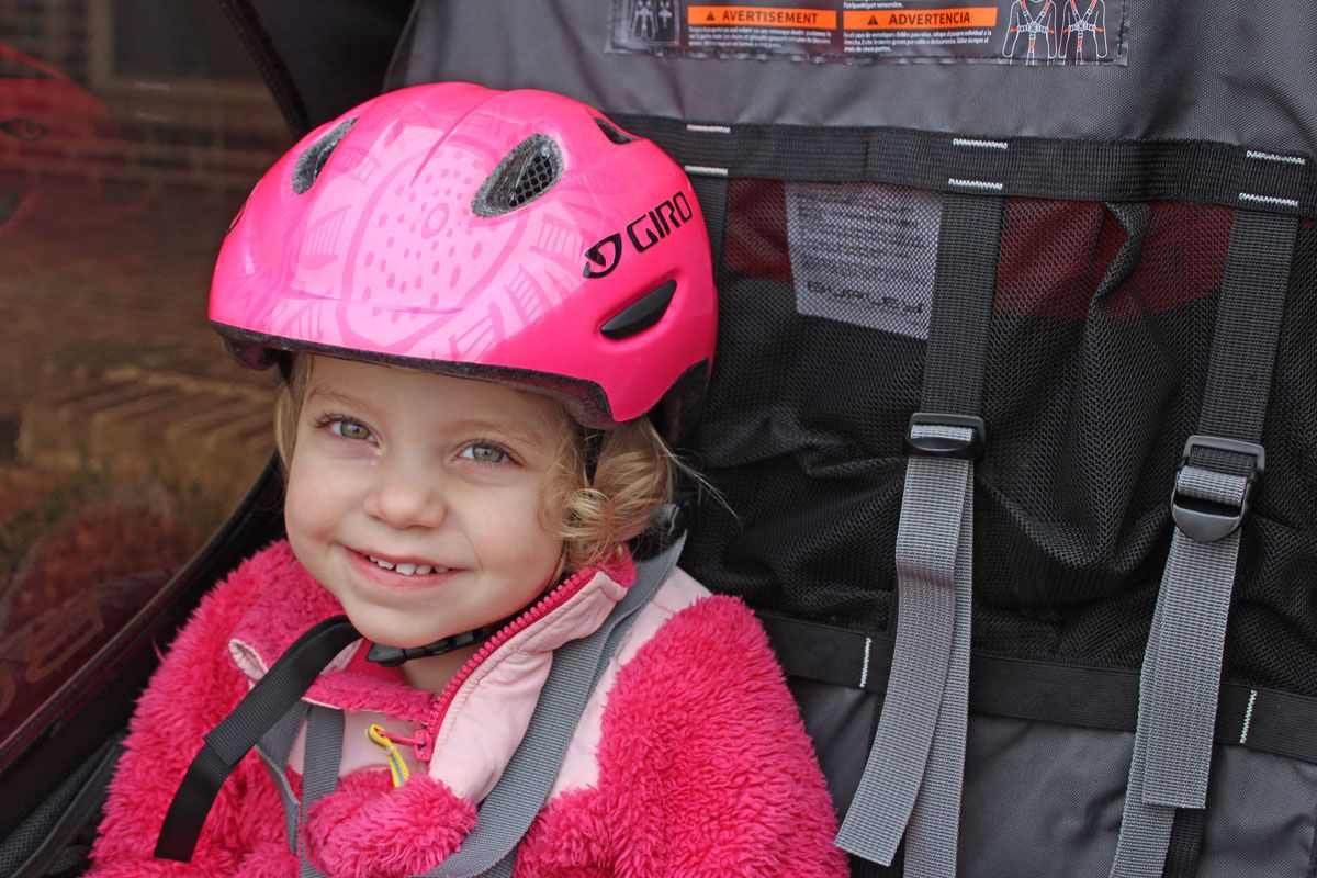 Toddler sitting in Burley Honey Bee bike trailer with mesh pocket behind her helmet.