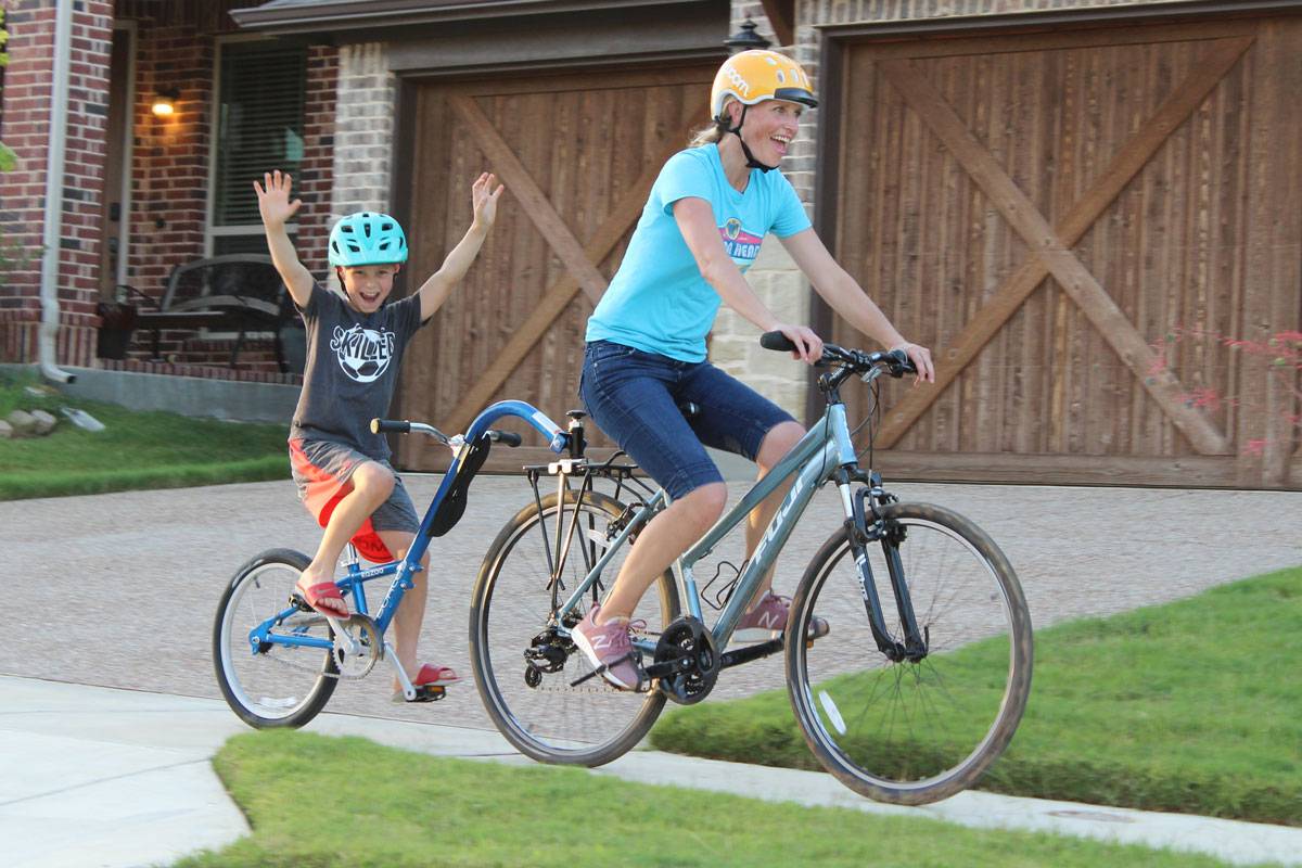Mom pulling 8-year-old on the Burley Kazoo trailer cycle - his hands are in the air