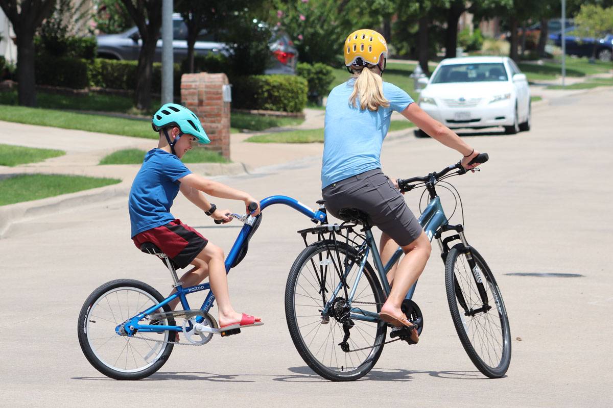 Mom pulling 8 year old boy on Burley Kazoo trailer cycle. Riding in the street, turning sharply.