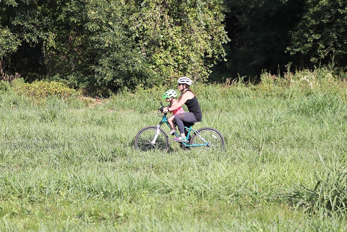 3 year old girl riding Do Little child bike seat with her mom through grassy field