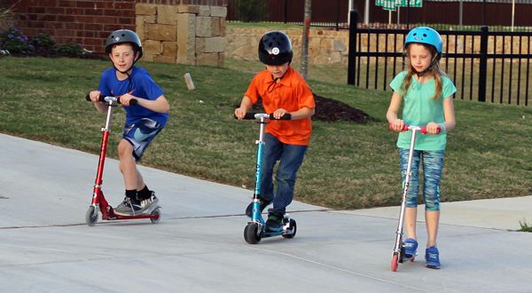 group of three kids riding different kick scooters for kids