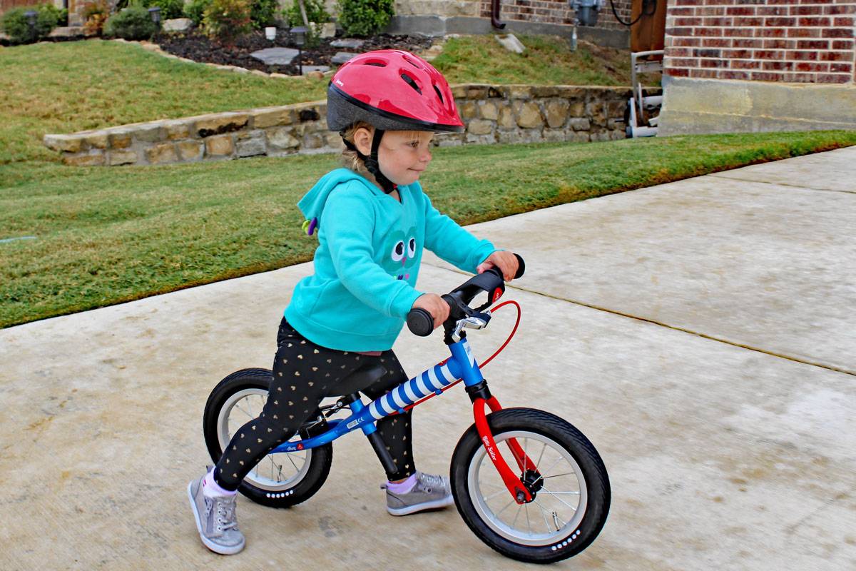 2 year old riding balance bike while wearing Joovy Noodle helmet