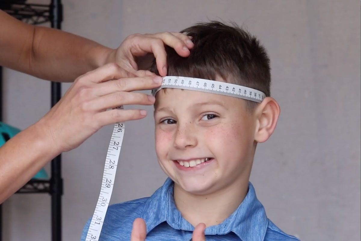 Mom measuring her son's head with a soft tape measure to determine the right kids bike helmet size