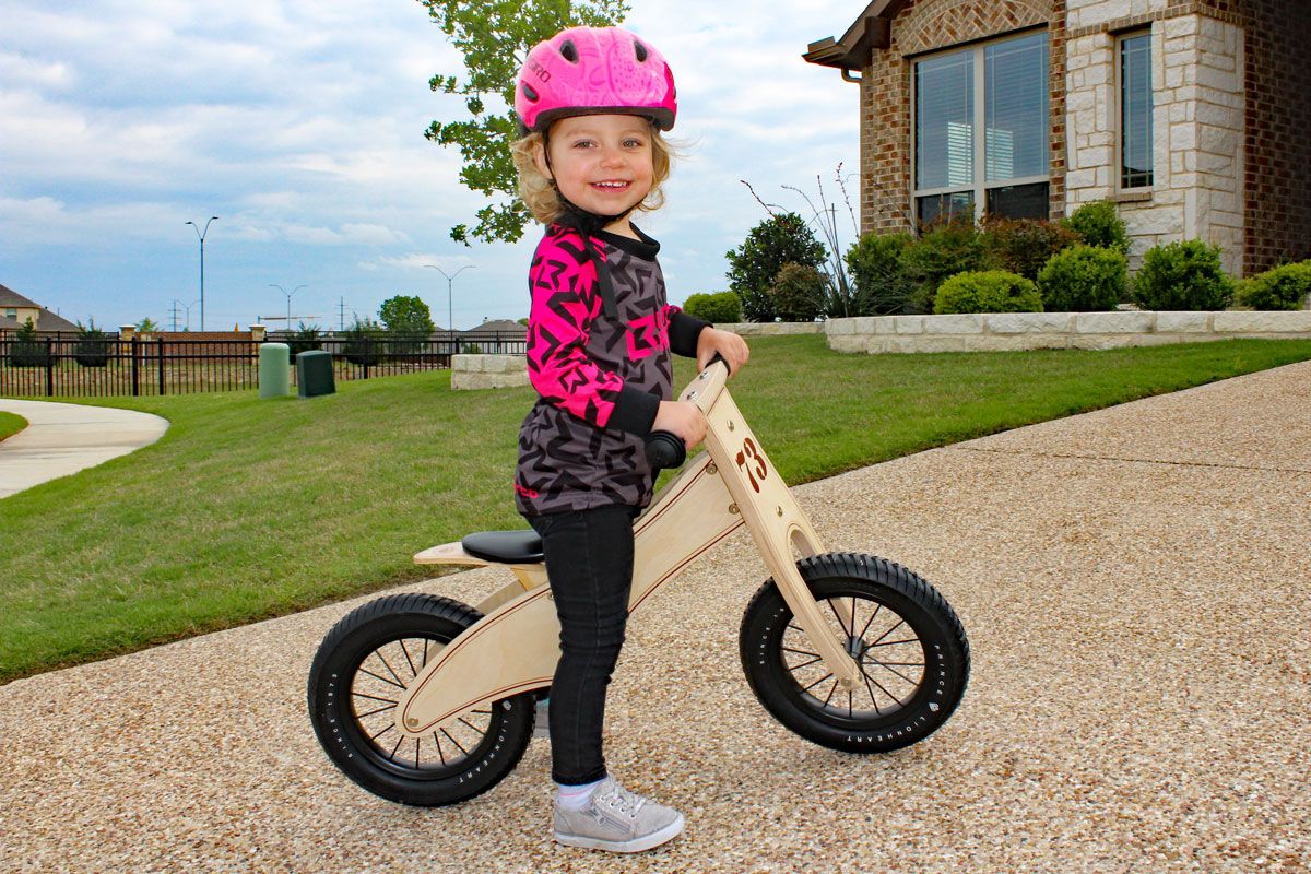 2 year old standing and smiling on Prince Lionheart wooden balance bike