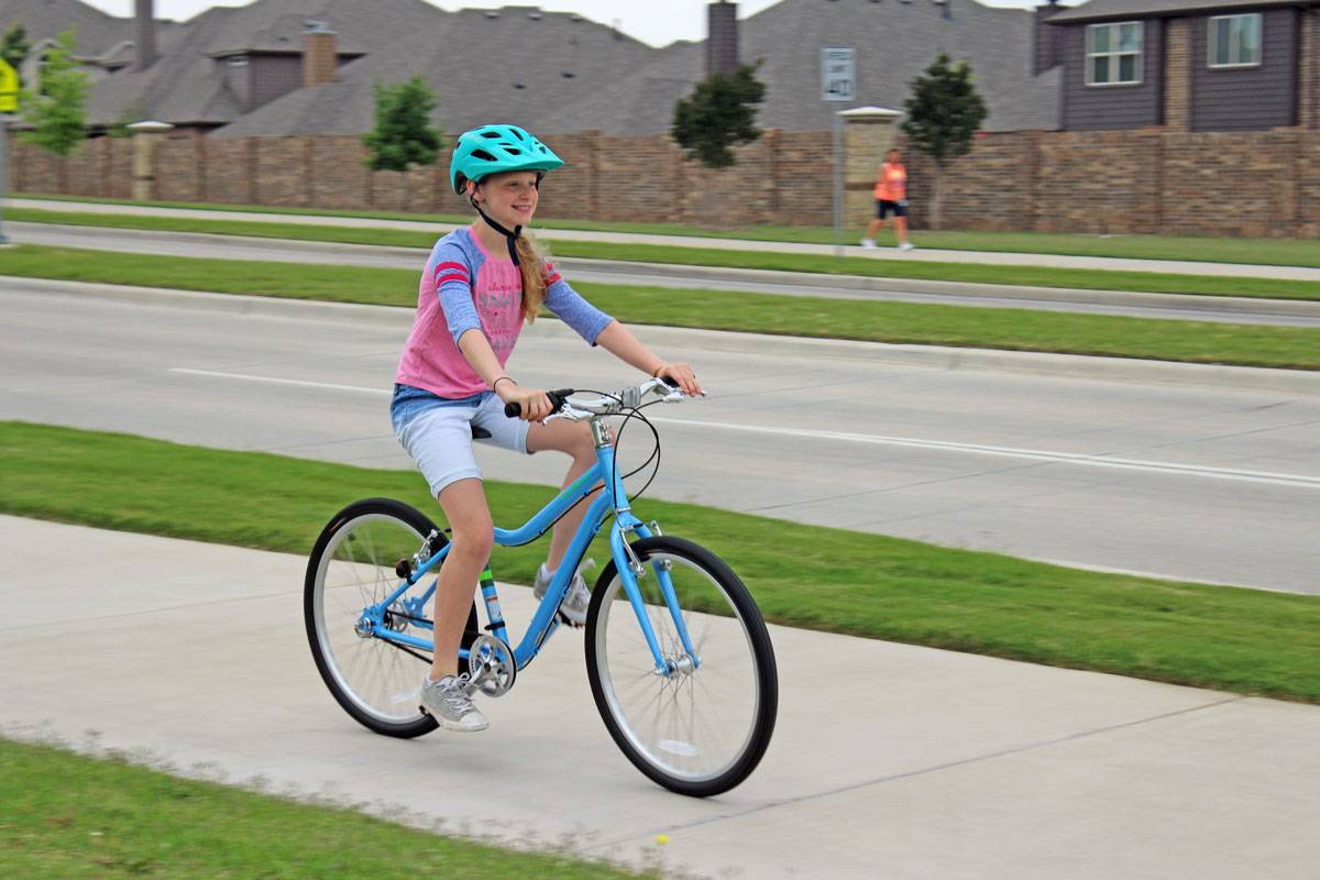 Girl riding Priority Bicycles Start 24 inch kid's bike on a street sidewalk