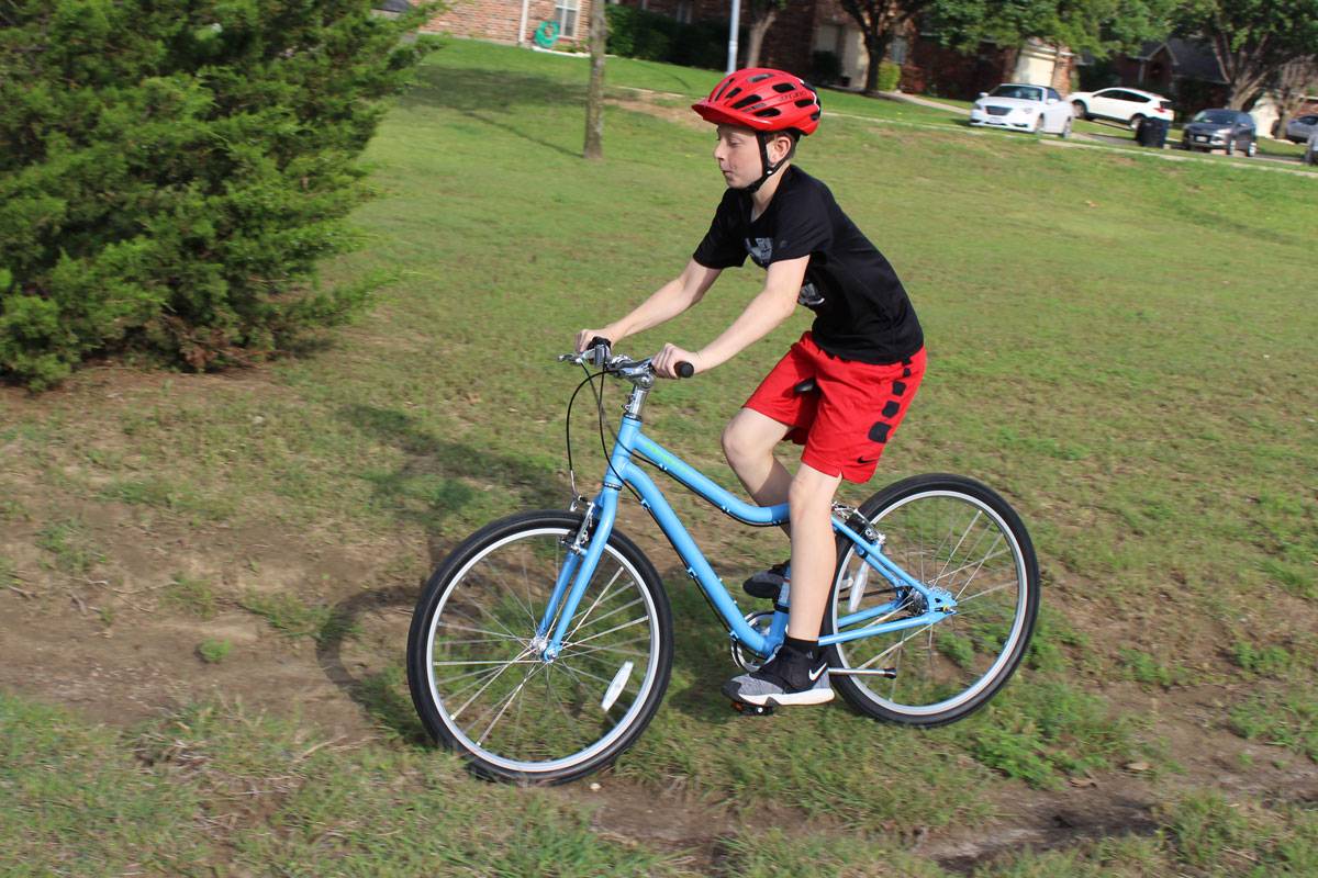 Boy riding Priority Start 24" kid's bike on a rough patch of dirt