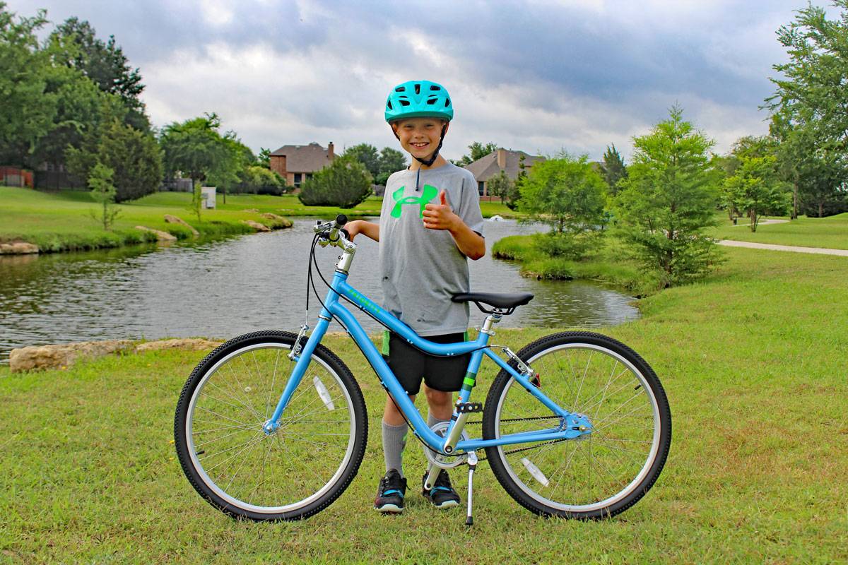 young riding standing next to the priority start 24 inch kids bike