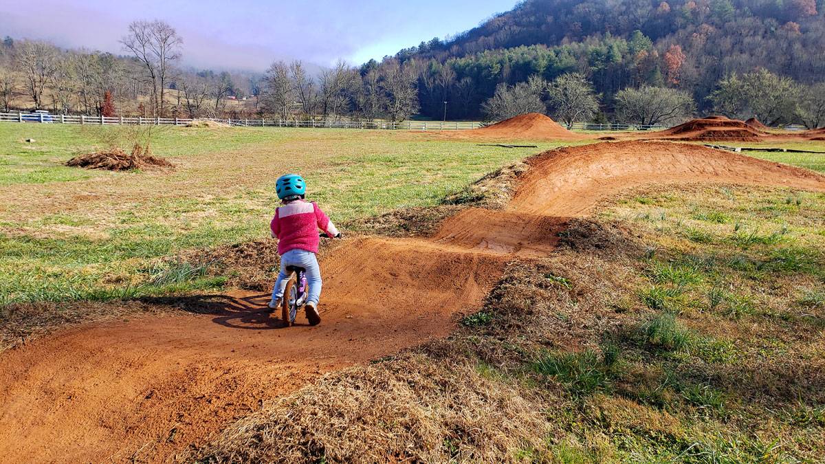 young toddler riding woom 1 balance bike on red dirt pump track.
