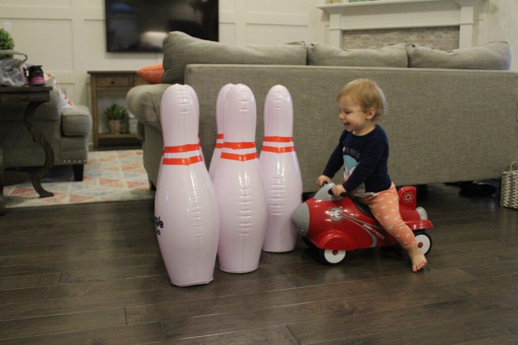 baby on Radio Flyer balance bike knocking over inflatable bowling pins