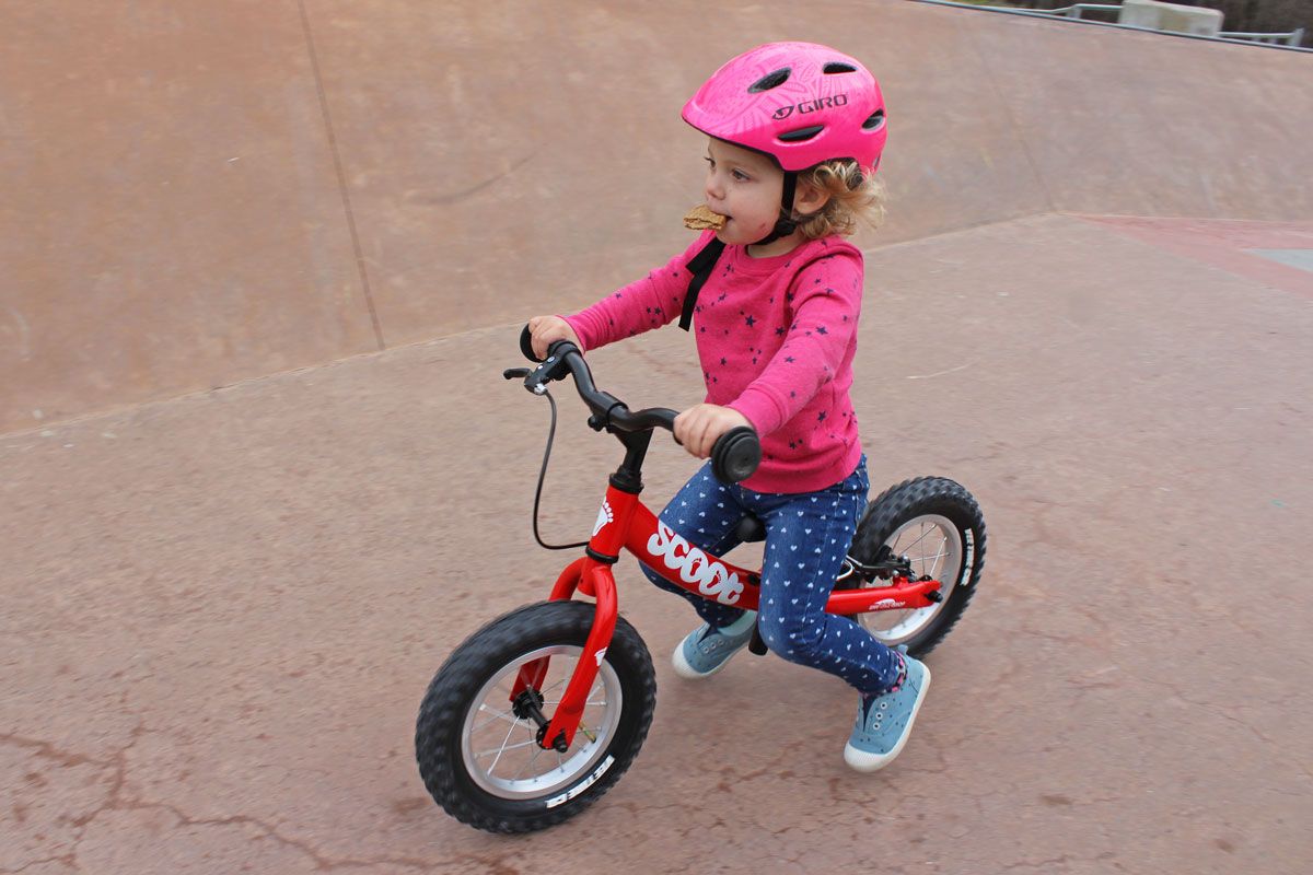 Toddler riding Ridgeback Scoot balance bike down a ramp at the skatepark while eating a cracker.