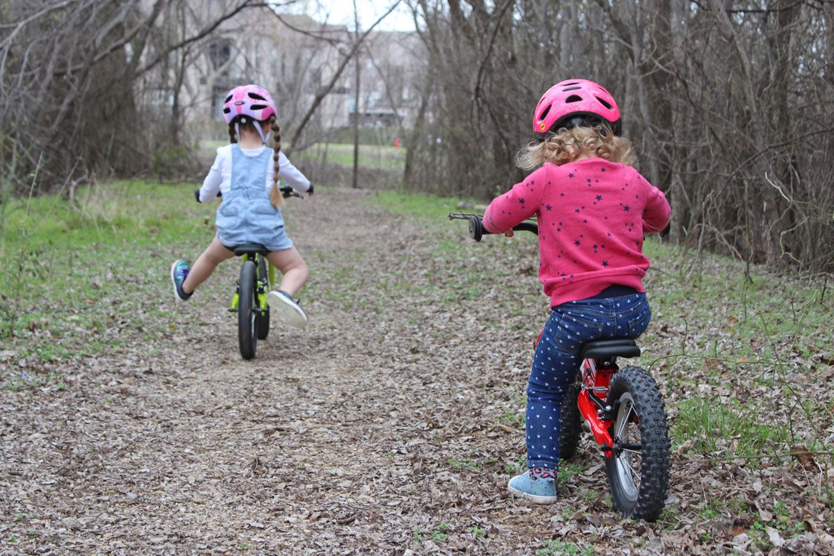 2 year old and 4 year old riding Ridgback Scoot XL balance bikes through the forest