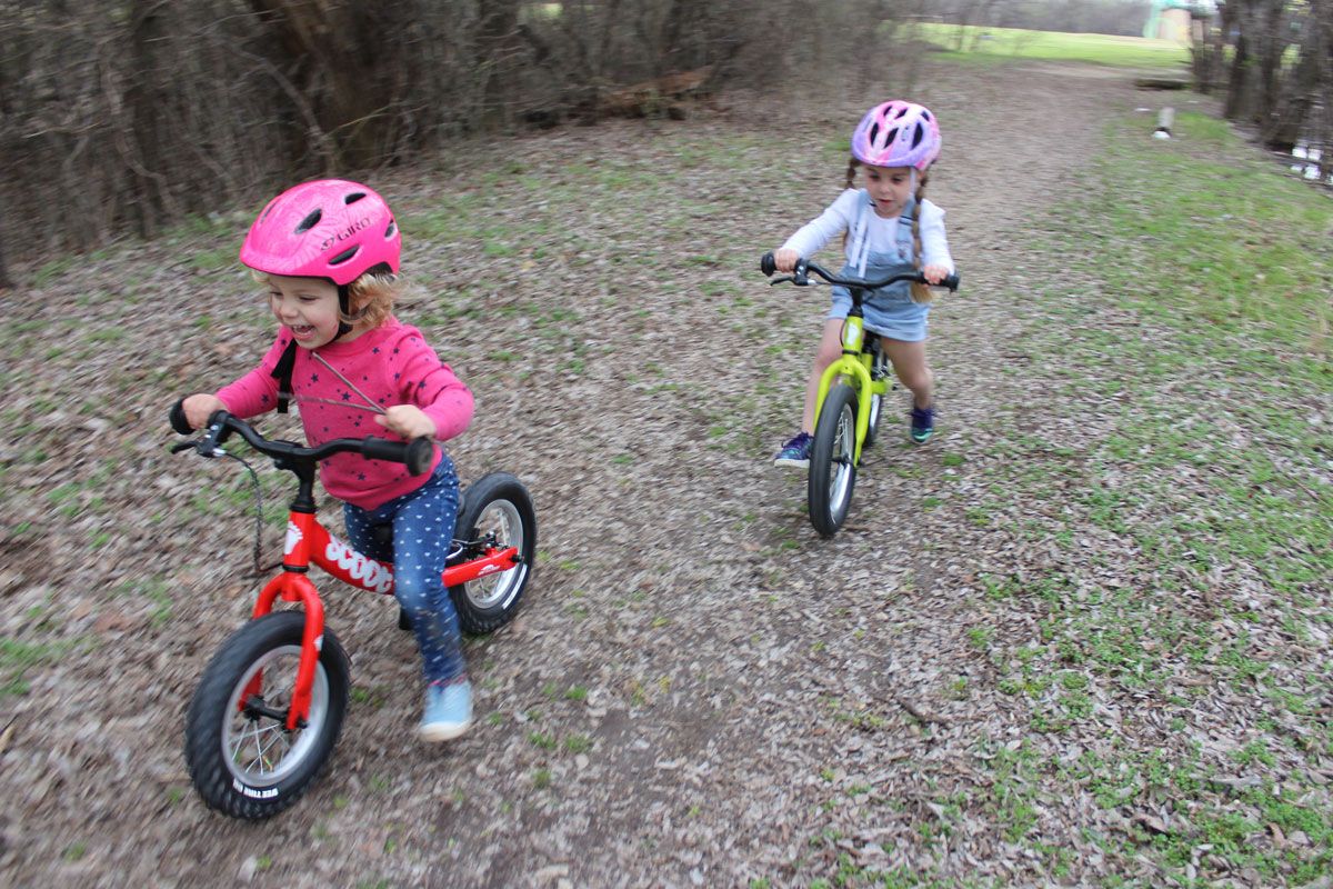 2 year old and 4 year old riding Ridgback Scoot XL balance bikes through the forest