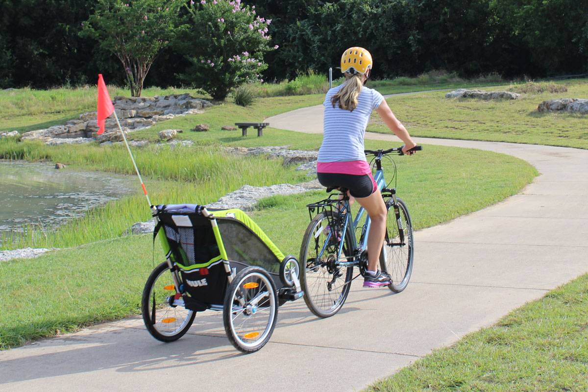 Mom pulling Thule Chariot Cheetah XT single bike trailer on paved trail by lake