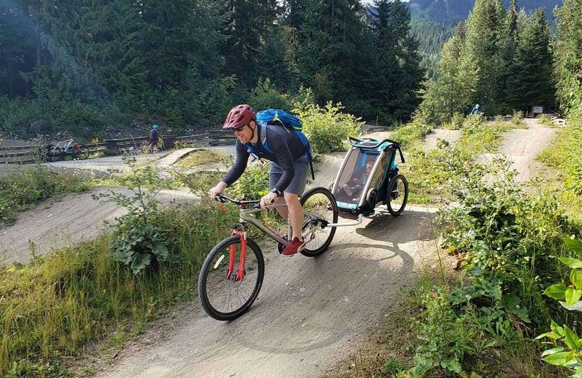 Dad pulling Thule Chariot Cross bike trailer on jump trails at Whistler bike park.