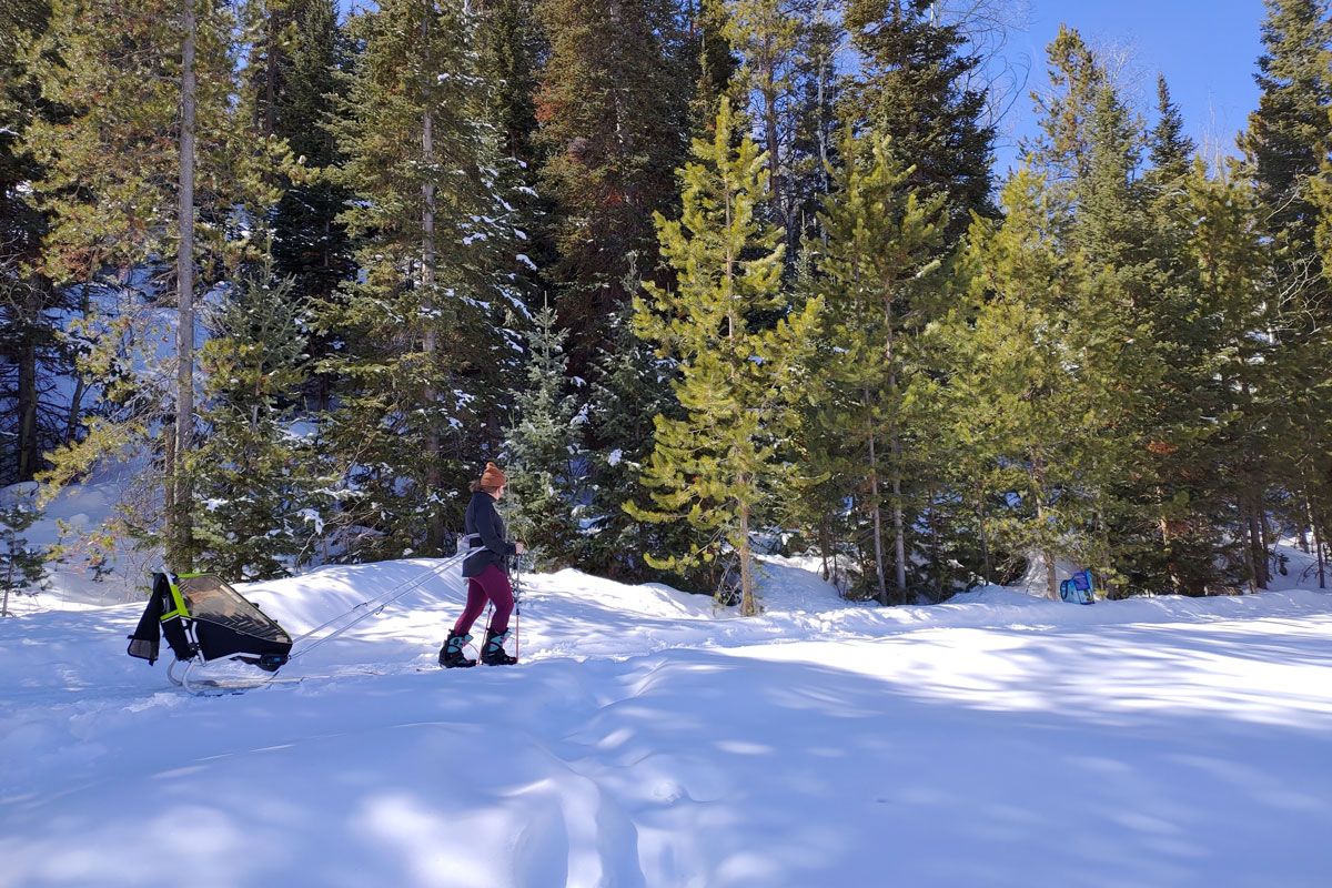 Mom pulling baby across snowing field with Thule Chariot Ski Kit.