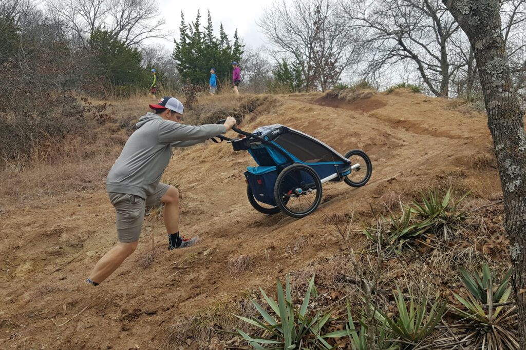 Man pushing Thule chariot Cross up a dirt hill in trailer mode.