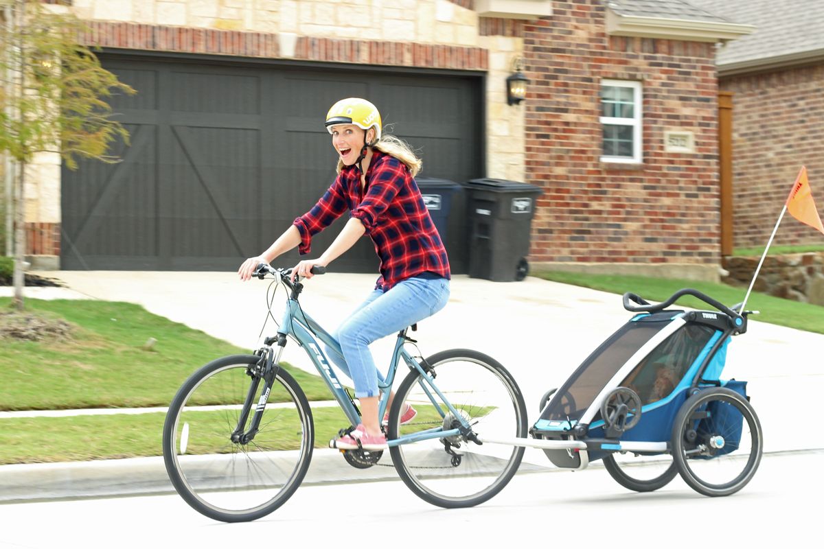 Mom riding bike while pulling the Thule chariot Cross bike trailer behind her