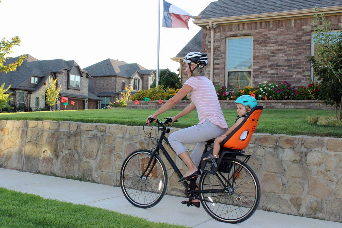 Mom riding with toddler in Thule Yepp Nexxt Maxi child bike seat down the sidewalk