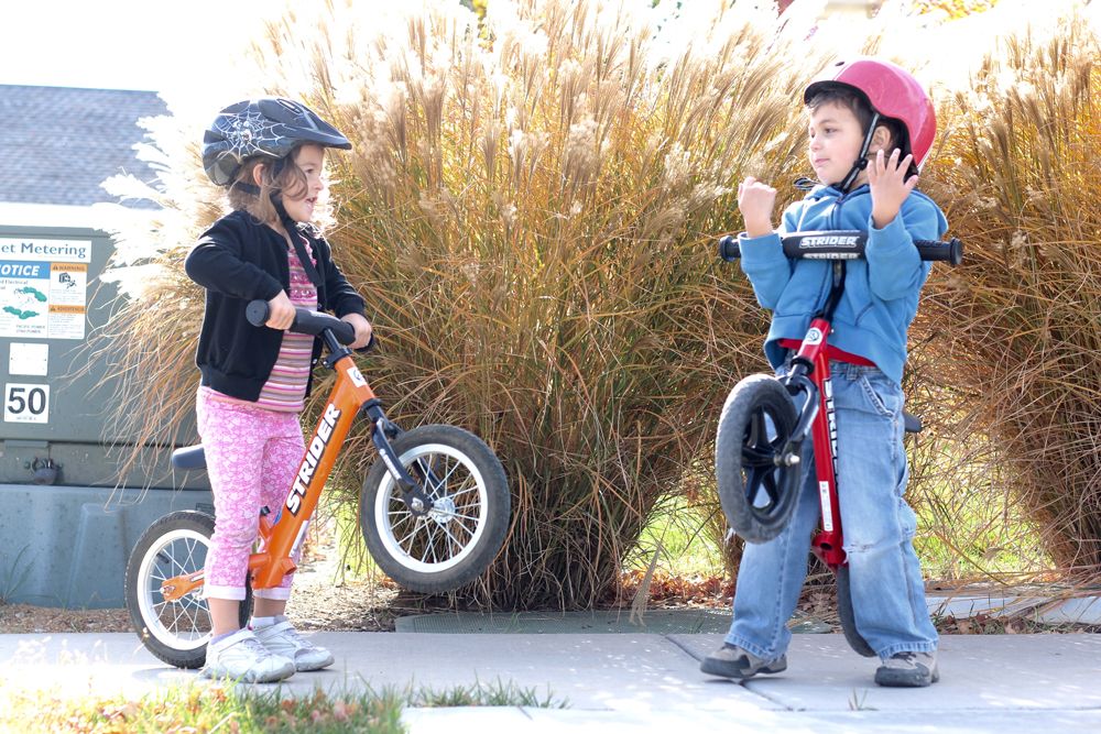 two preschoolers lifting up their Strider balance bikes while talking to each other.