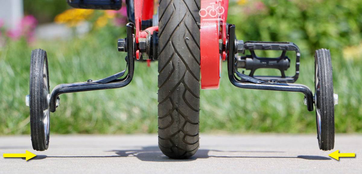 Rear view of a kid's bike with training wheels. The Training wheels are even with each other, but don't touch the ground.