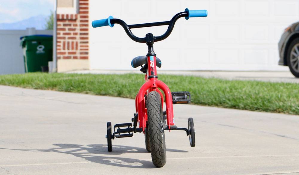 12" kid's bike with training wheels, tilted to one side as it leans on one training wheel.