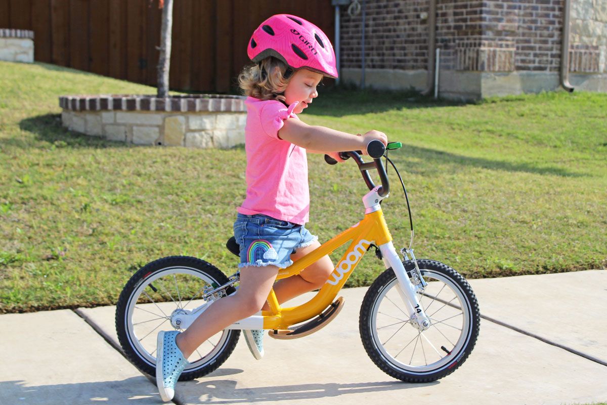 2 year old riding woom 1 plus balance bike down sidewalk