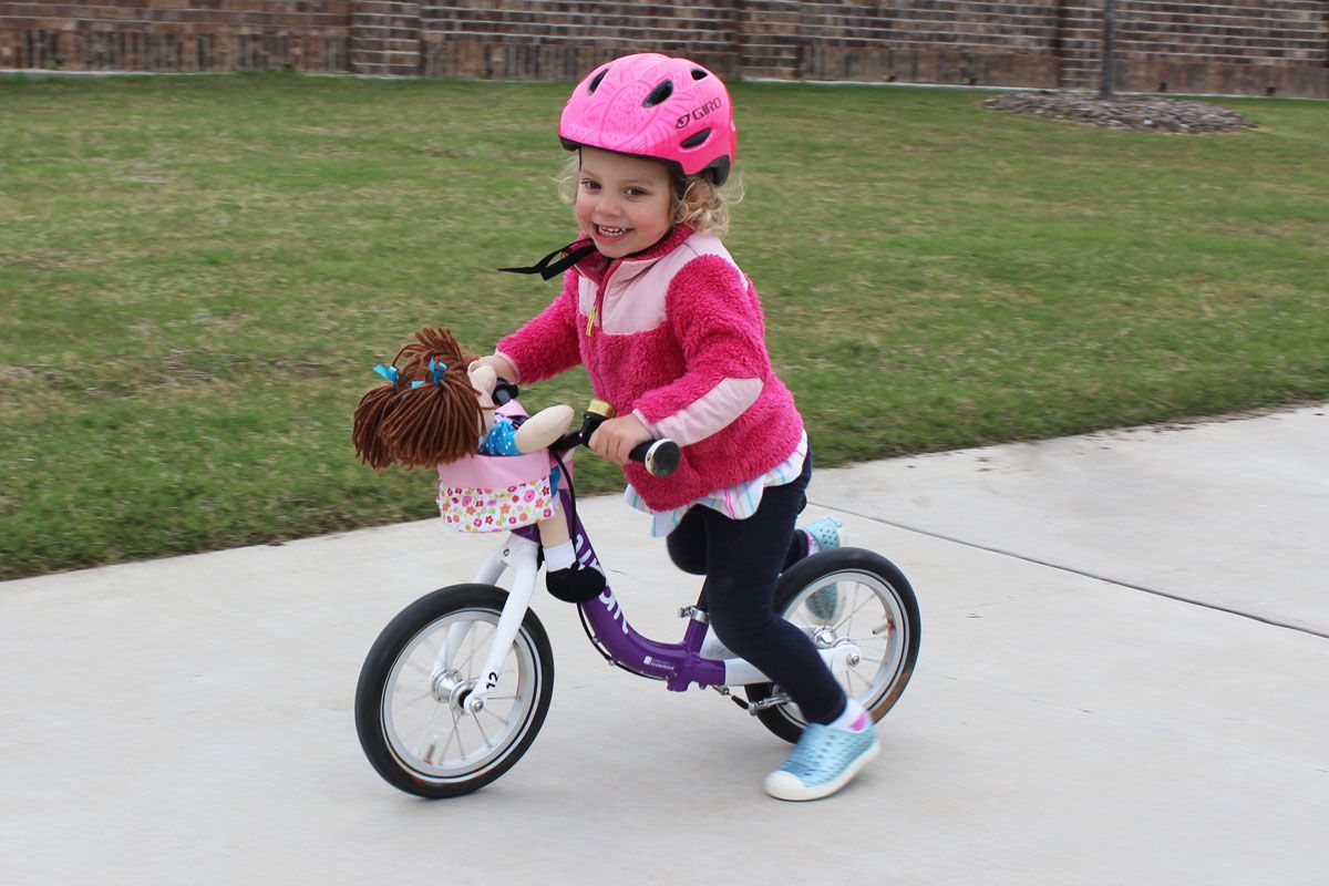 toddler riding woom 1 balance bike with her dolly in the Haba doll bike seat
