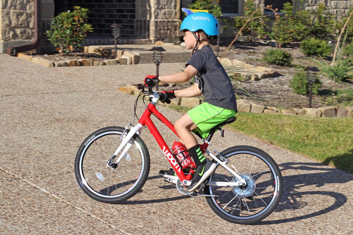 a boy riding a red woom bike on the driveway
