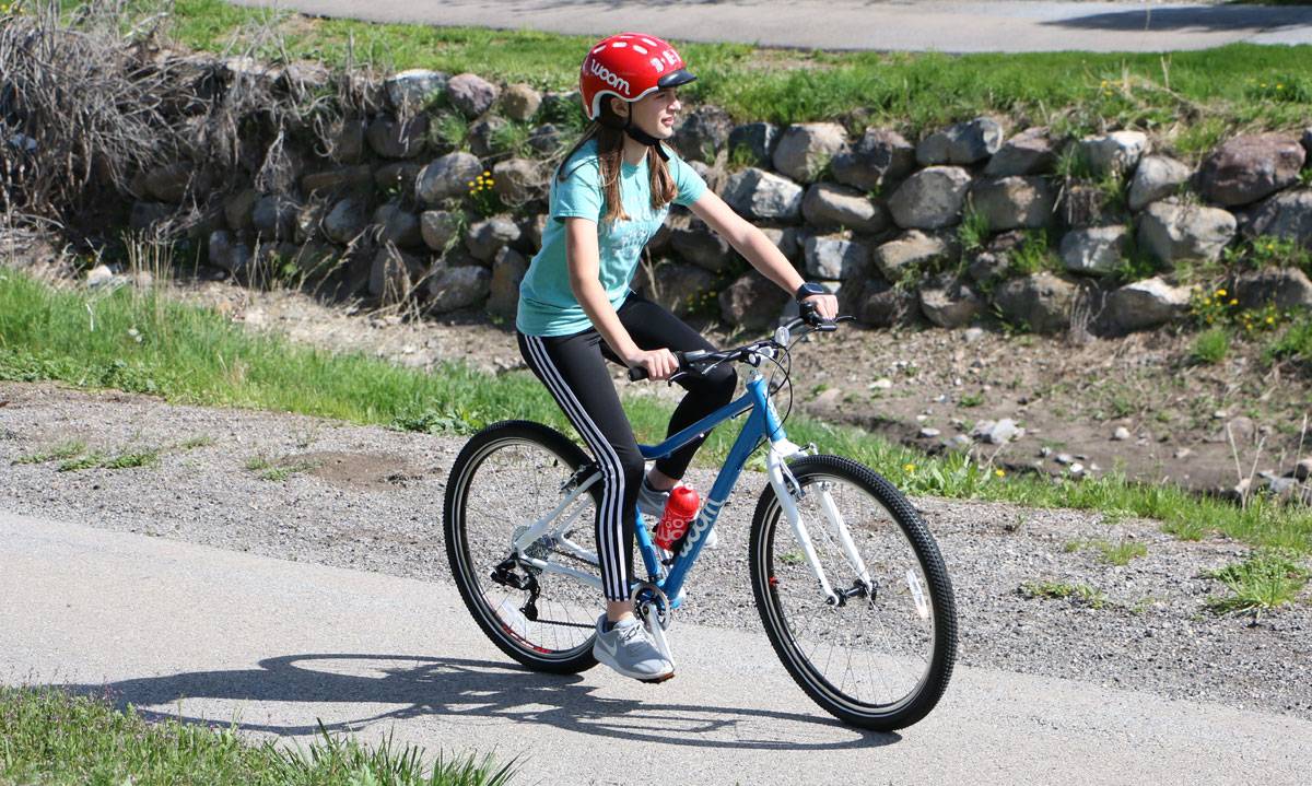 tween girl riding the woom 6 kid's bike down a paved trail
