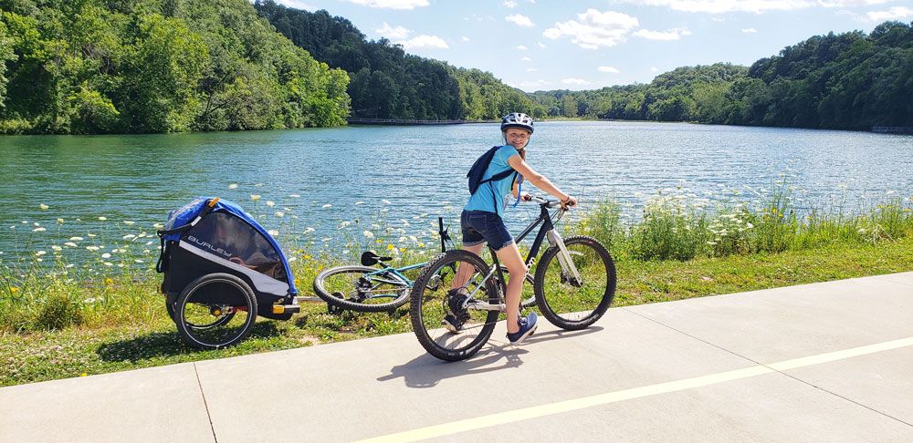 girl standing on her bike with a burley d'lite bike trailer in front of Lake Atalanta in Rogers, Arkansas
