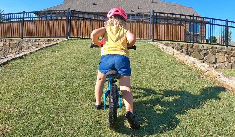 Toddler riding Vitus Smoothy balance bike up a grass hill