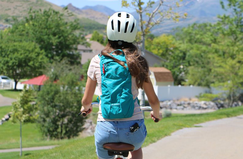 Young girl riding her bike while wearing a teal Osprey kitsuma 3 hydration pack
