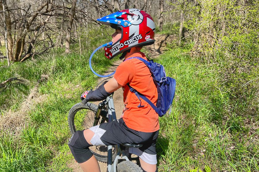 Boy mountain biking and drinking from the Outdoor Products Tadpole hydration pack for kids